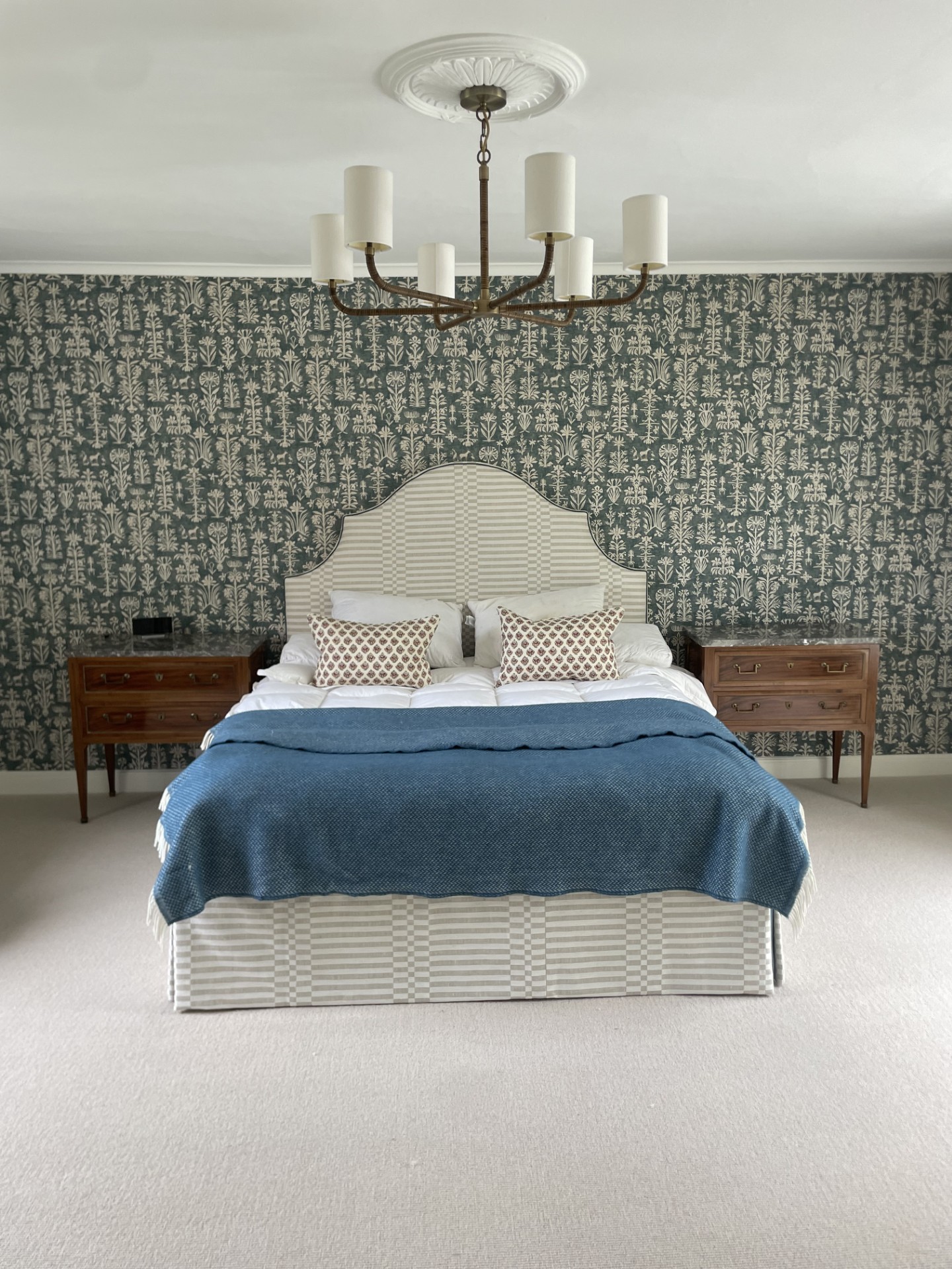 Bedroom with patterned wallpaper behind the bed and a chandelier