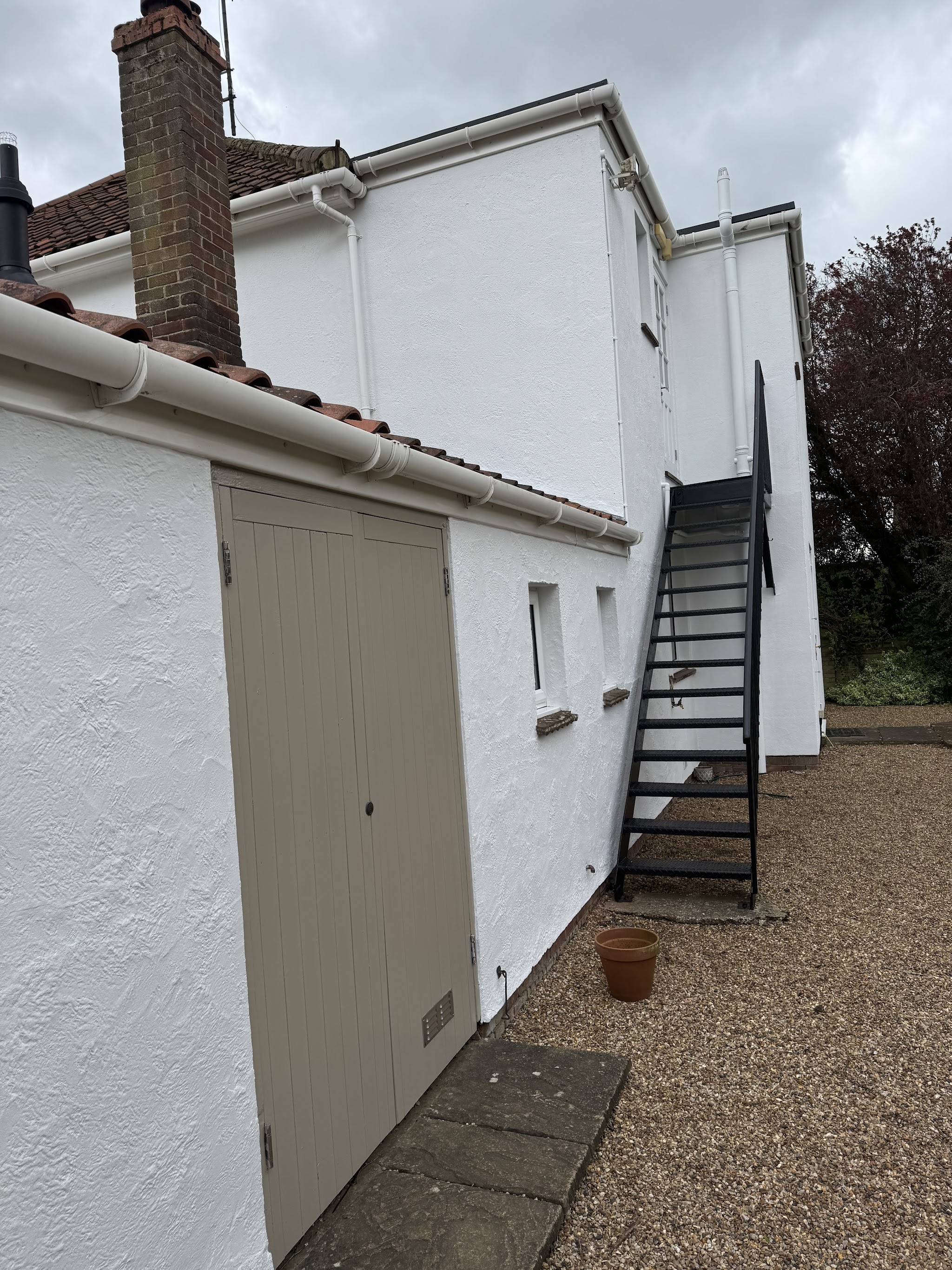 White rendered house with a taupe painted door and iron staircase